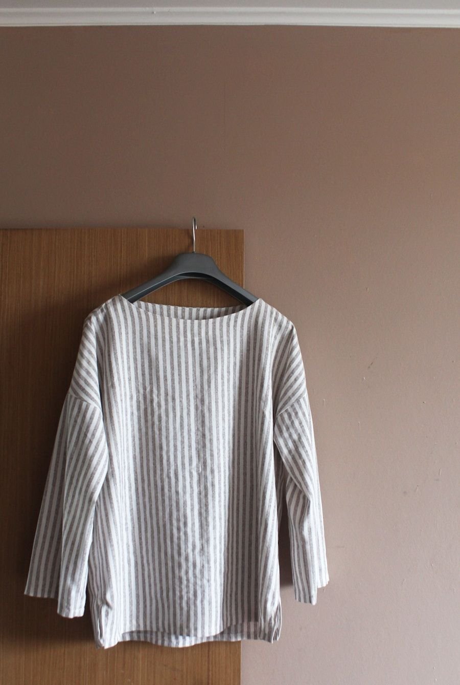 Fine striped silk shirt hanging from a wooden hanger against a warm taupe wall