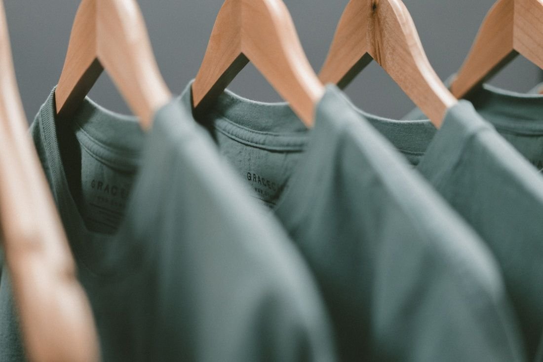 Row of finished sage-green garments on wooden hangers seen close up