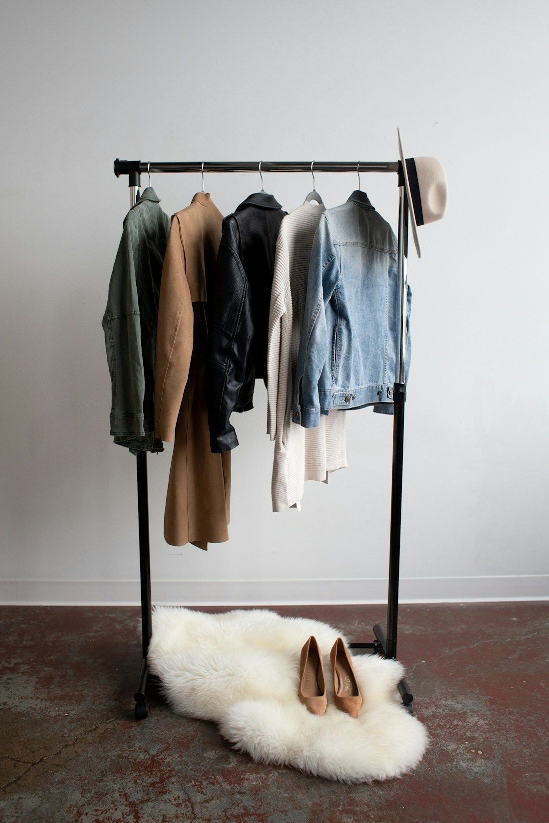 Quiet corner of an atelier with a slim rail of finished garments and a sheepskin on the floor
